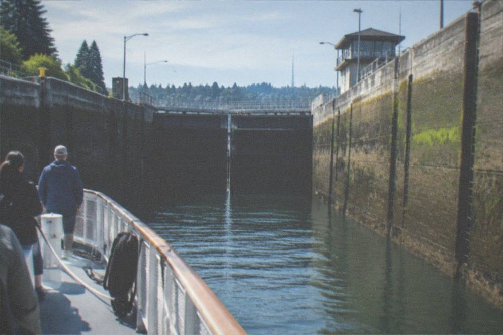 A tour boat inside the Ballard Locks chamber with gates closed and the wall rising above the deck