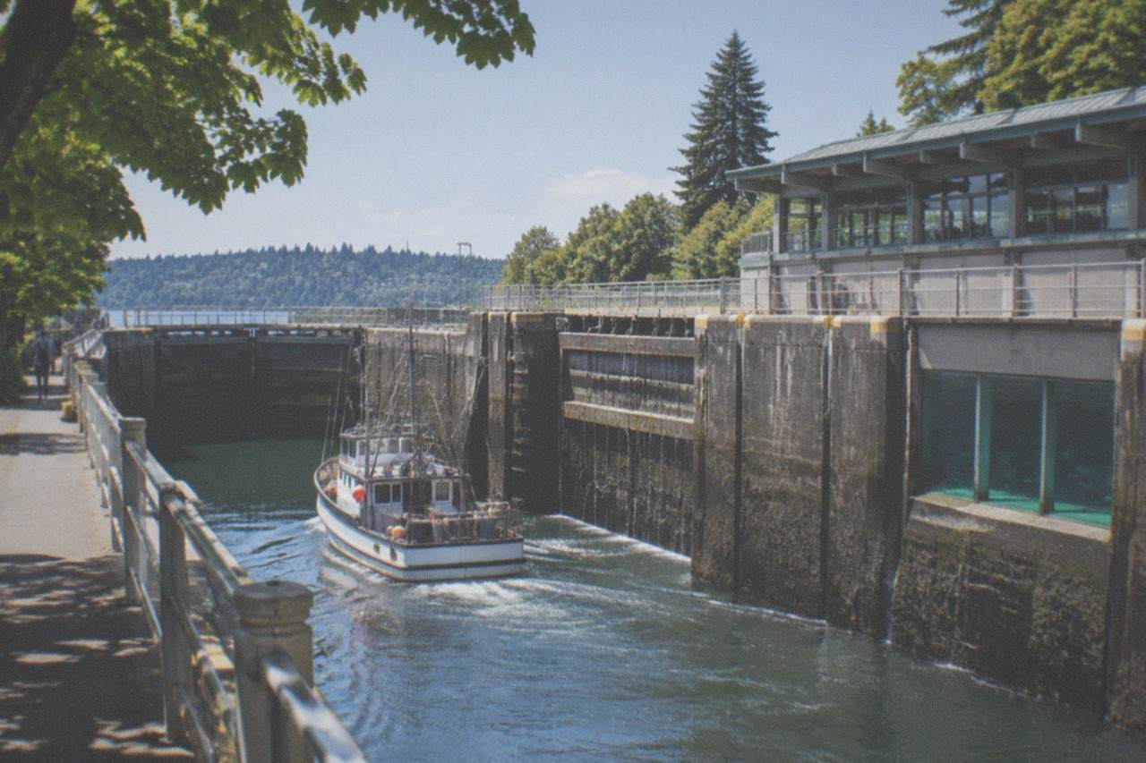 A boat passing through the large lock chamber at the Ballard Locks with the salmon ladder viewing building alongside