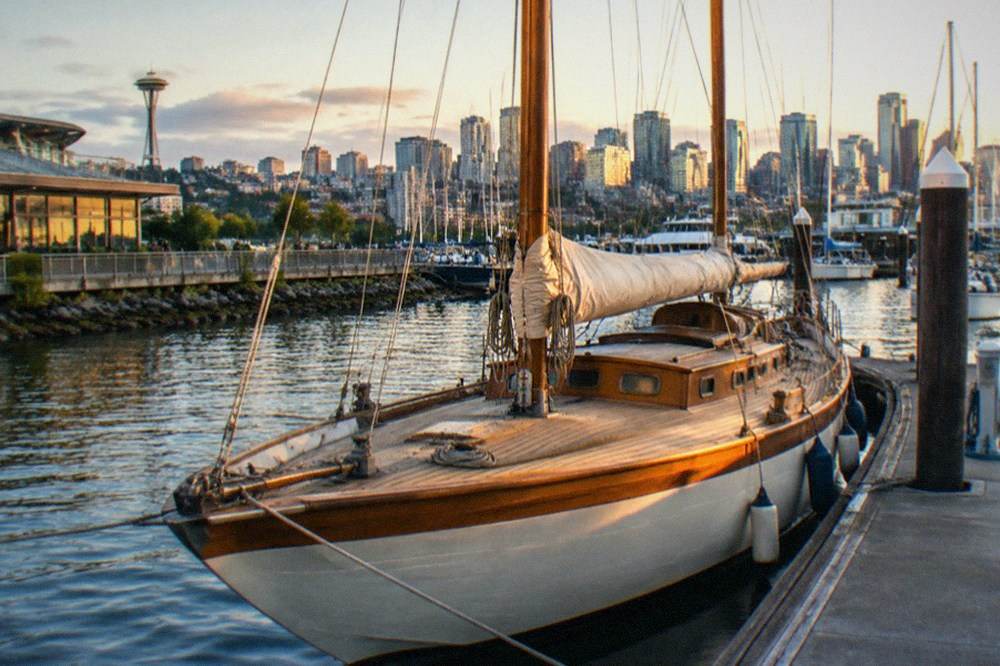 A classic sailboat with tall masts moored at a Seattle marina in warm evening light.
