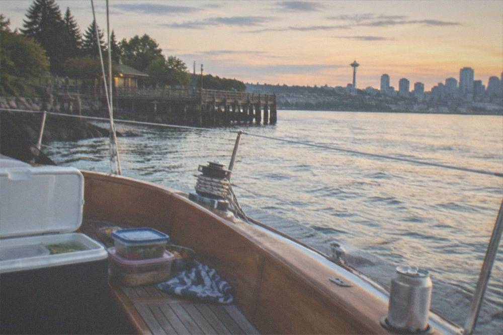 Soft cooler and reusable food containers open on a wooden sailboat bench with the Seattle skyline across the water