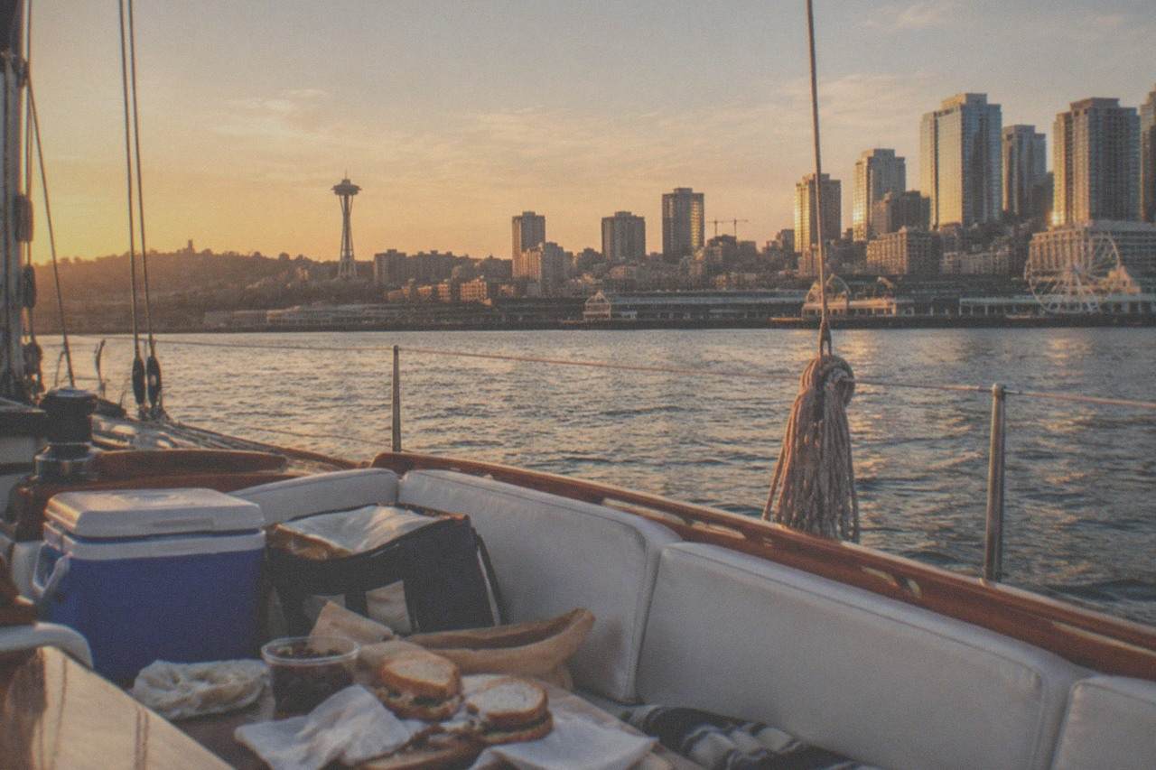 Sailboat deck on Elliott Bay at golden hour with a cooler and picnic supplies set out on the seating