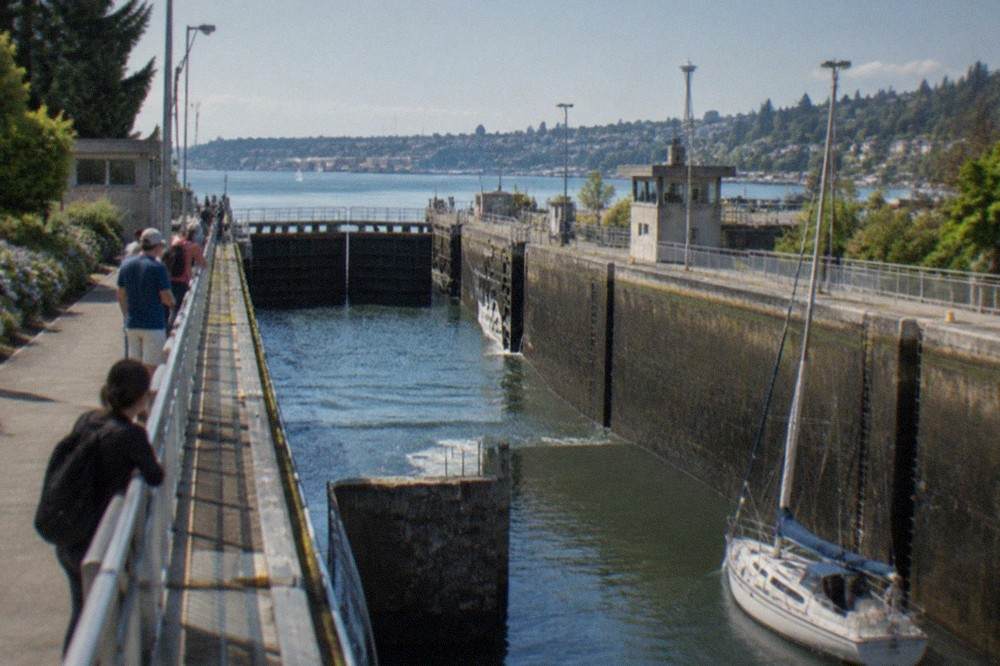 Visitors standing on the walkway beside the large lock chamber as a sailboat passes below