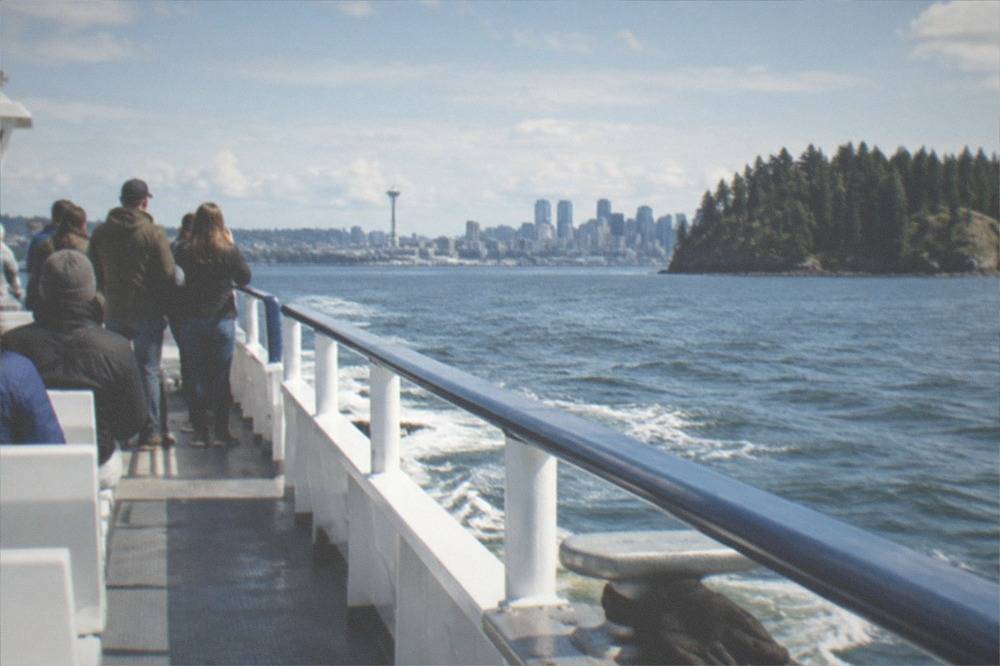 A whale watching boat with passengers on the observation deck traveling across open water near forested islands