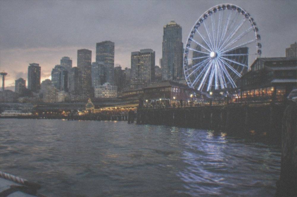 Ferris wheel and pier buildings along the Seattle waterfront seen across Elliott Bay at dusk