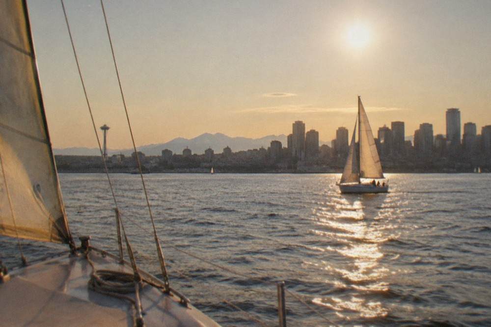 A sailboat on Puget Sound with the Seattle skyline behind it during a long summer evening