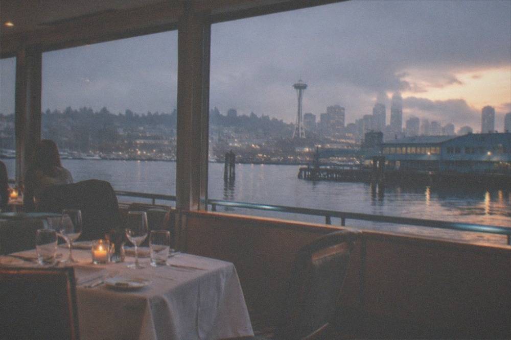 A set dinner table with glassware and candles inside a boat salon, with dusk light on Lake Union through the windows