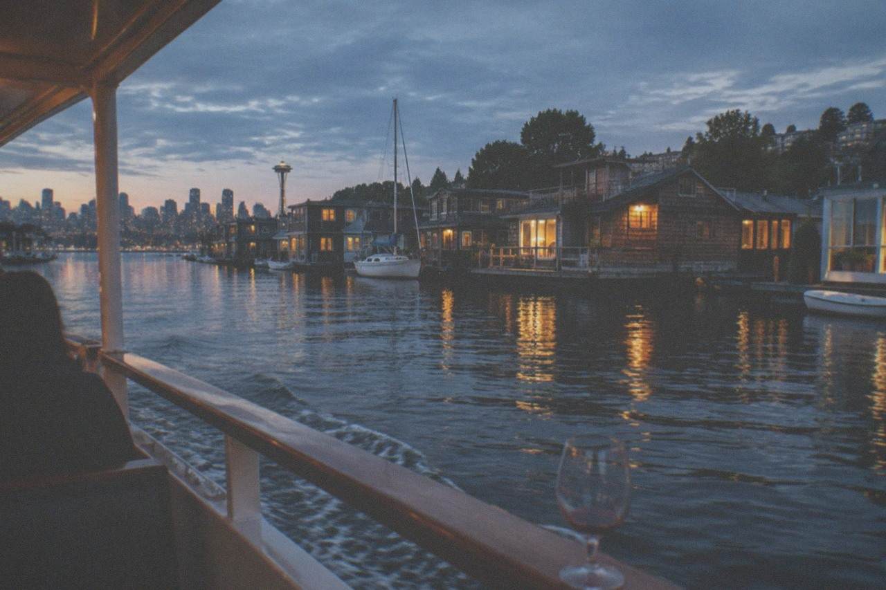 A covered dinner cruise boat on Lake Union at dusk, with Seattle houseboats and city lights along the shore