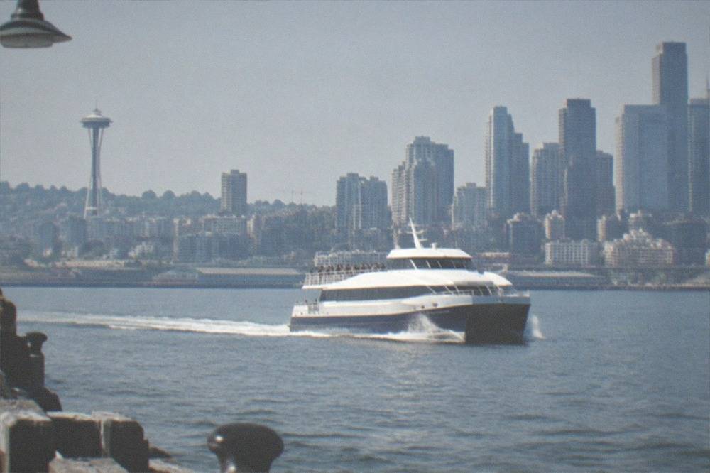 A fast catamaran whale watching vessel cruising past Seattle's skyline on Puget Sound