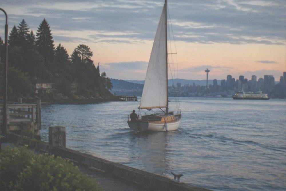 A classic sailboat under way near Bainbridge Island with forested shoreline and moored boats
