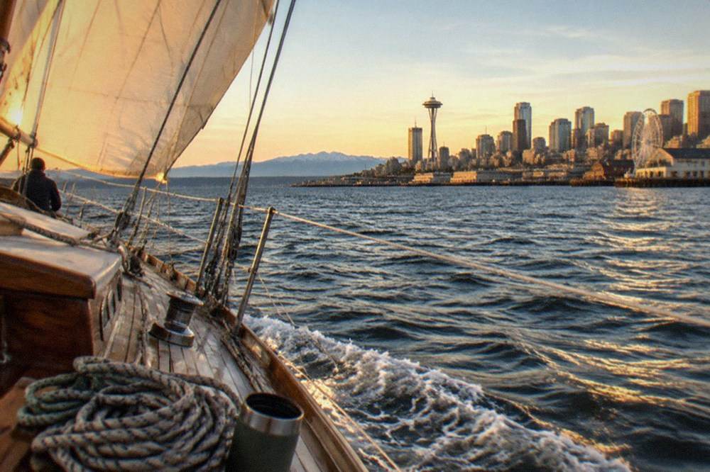 A sailboat heeling on Puget Sound at sunset with the Olympic Mountains on the horizon