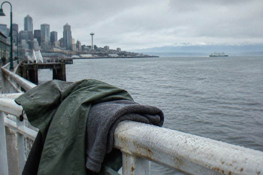 A rain jacket and folded fleece resting on a boat rail with gray water and distant mountains beyond