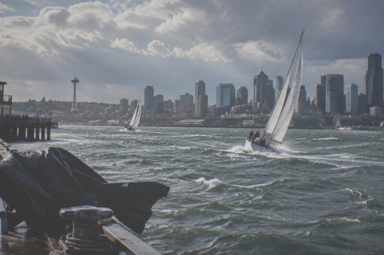 Sailboats on Elliott Bay with the Seattle skyline behind them under a partly cloudy sky