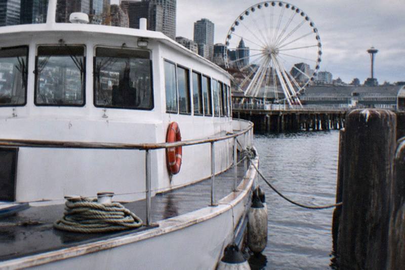 A sightseeing boat on Elliott Bay near the downtown Seattle waterfront, the category card for harbor cruises: two one-hour guided trips run by Argosy Cruises, boarding at Pier 55 with seasonal departures at Pier 54, from $43 per person.