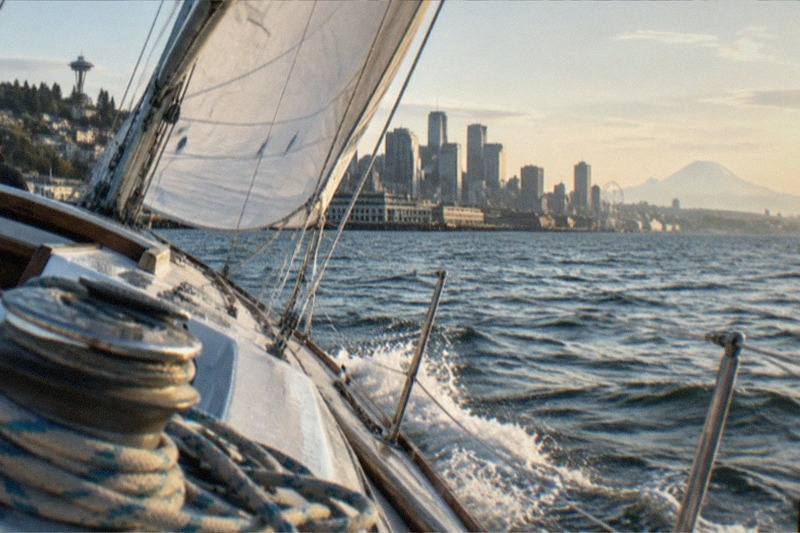 Sailboat heeling with sails set on Puget Sound, downtown Seattle in the background; the sailing category spans five trips from $50 per person, from 70ft BYOB boats to two Bainbridge Island options priced per group.