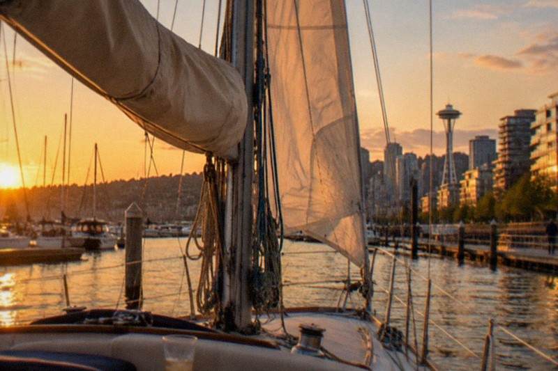 Tall ship under full sail at golden hour on Puget Sound, the Seattle skyline behind; the sunset-cruise category gathers four evening trips from $65 per person, run by Seattle's Tall Ship, Sailing Seattle and Argosy Cruises.
