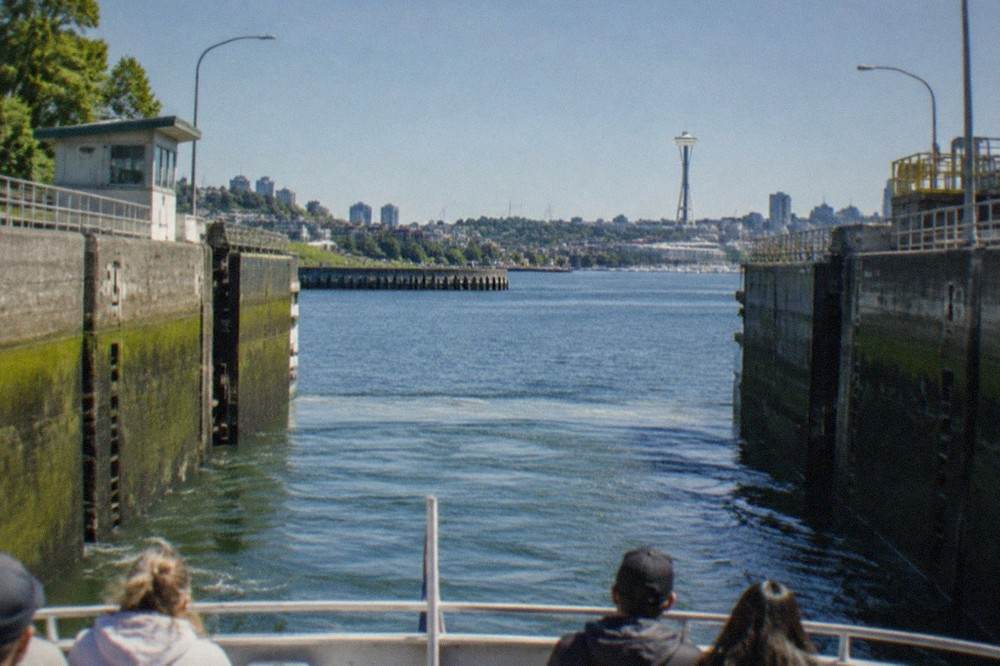 A small passenger vessel entering the open gates of a large lock chamber between concrete walls