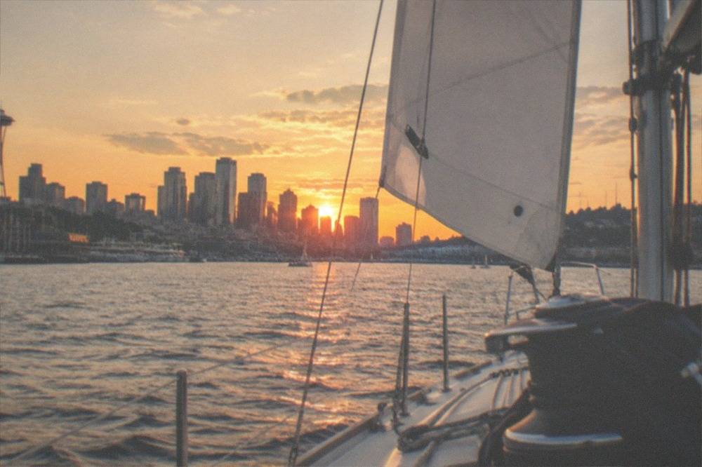 A sailing cruise passing the Seattle skyline as the sky turns orange at sunset