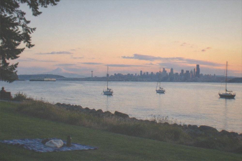 Sailboats on Elliott Bay under a long summer evening sky behind the Seattle skyline