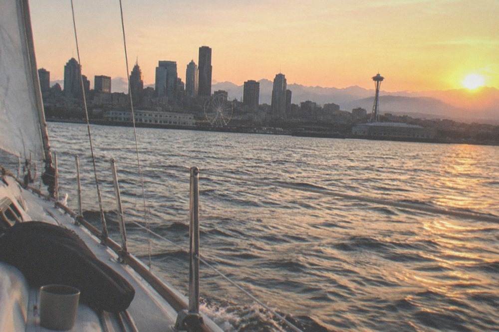 Sailboat heeling slightly on Elliott Bay with the sun low over the Olympic Mountains