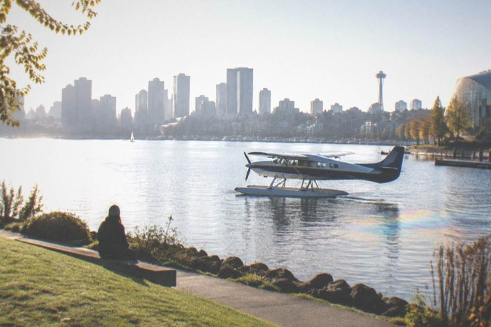 A seaplane floating on Lake Union water with the Seattle skyline behind it