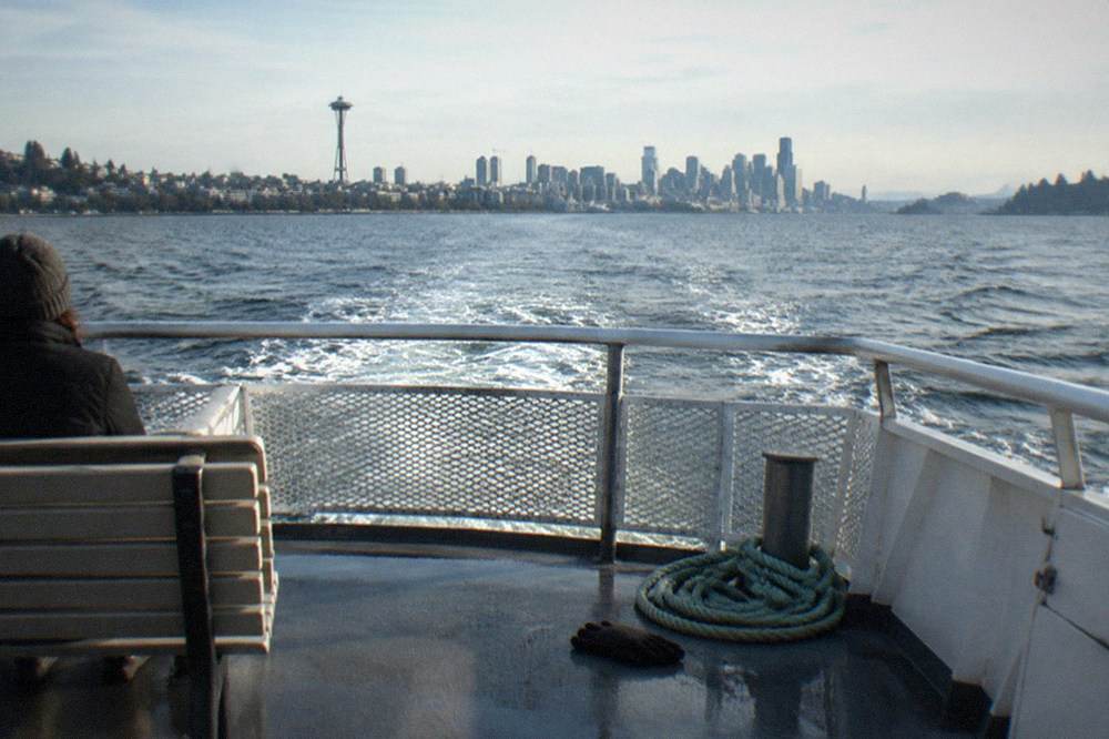 A cruise boat crossing open water toward Lake Washington with evergreen shoreline on the horizon