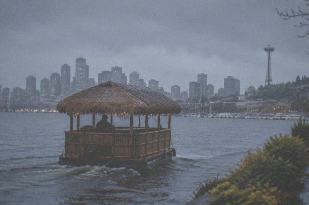 A thatched tiki style boat cruising across Lake Union at dusk with the skyline behind