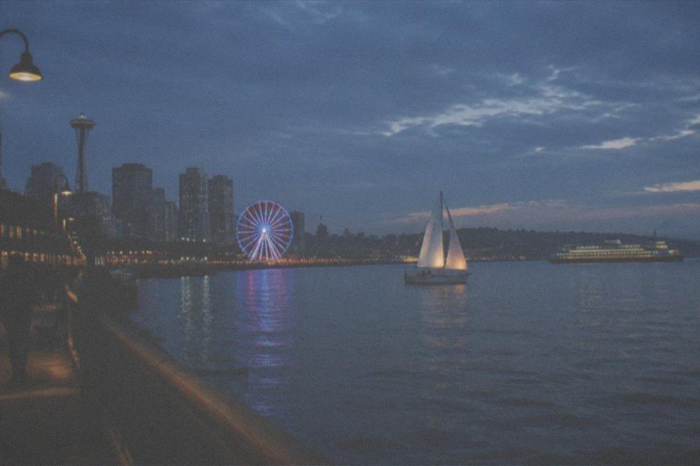 Sailboat and ferry sharing the water near the Seattle waterfront at dusk