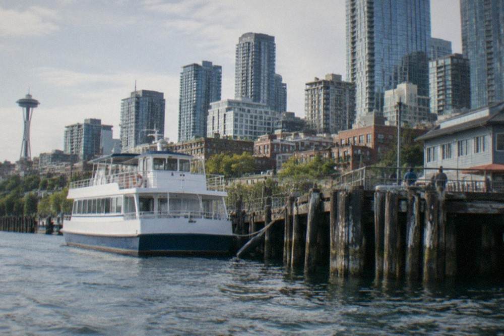 Tour boats moored at a downtown Seattle pier with the skyline rising above Elliott Bay