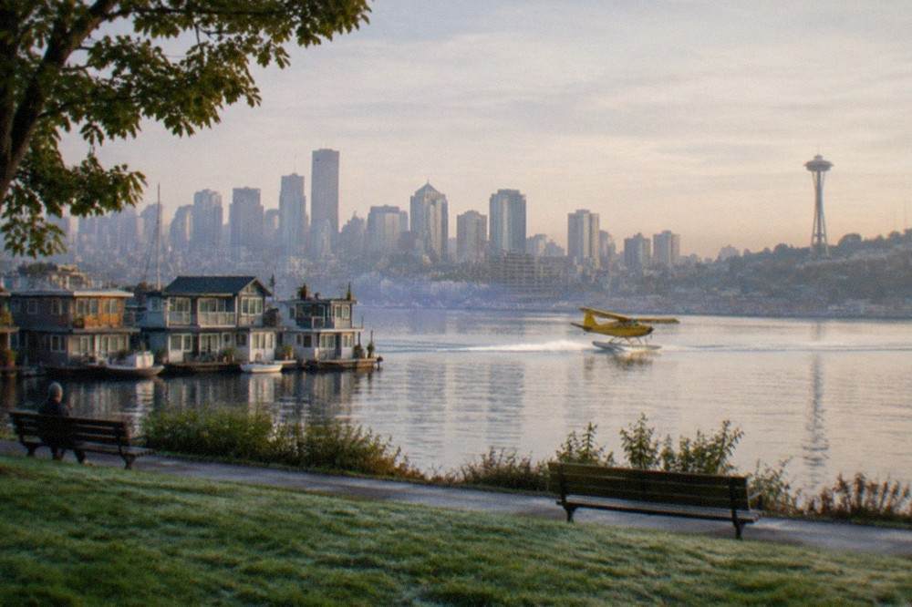 A floatplane lifting off Lake Union with the Seattle skyline and Space Needle behind it