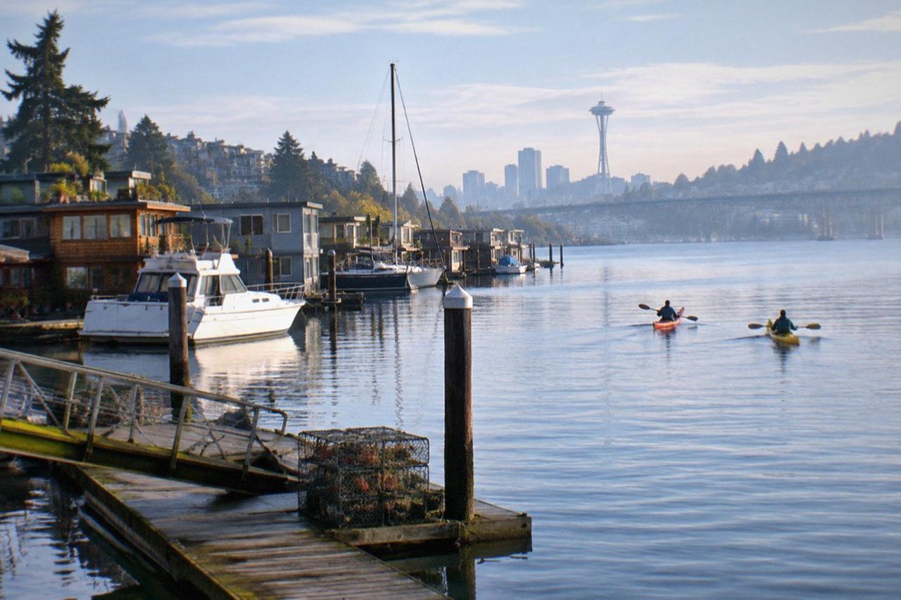 Chartered boat on calm Lake Union water with floating homes along the shore; the private-charter hub walks through four bookings, three priced per group from $289, covering floating homes tours, BYOB sightseeing and a tiki boat for up to 15.