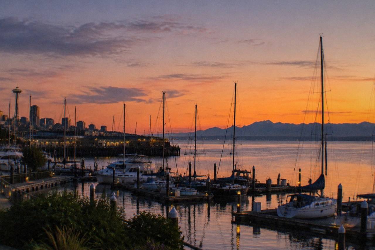 Sunset colors over Puget Sound as a sailboat passes the Seattle skyline; the sunset-cruise hub lines up four evening trips from $65 per person, most running April through October while evenings stay light.
